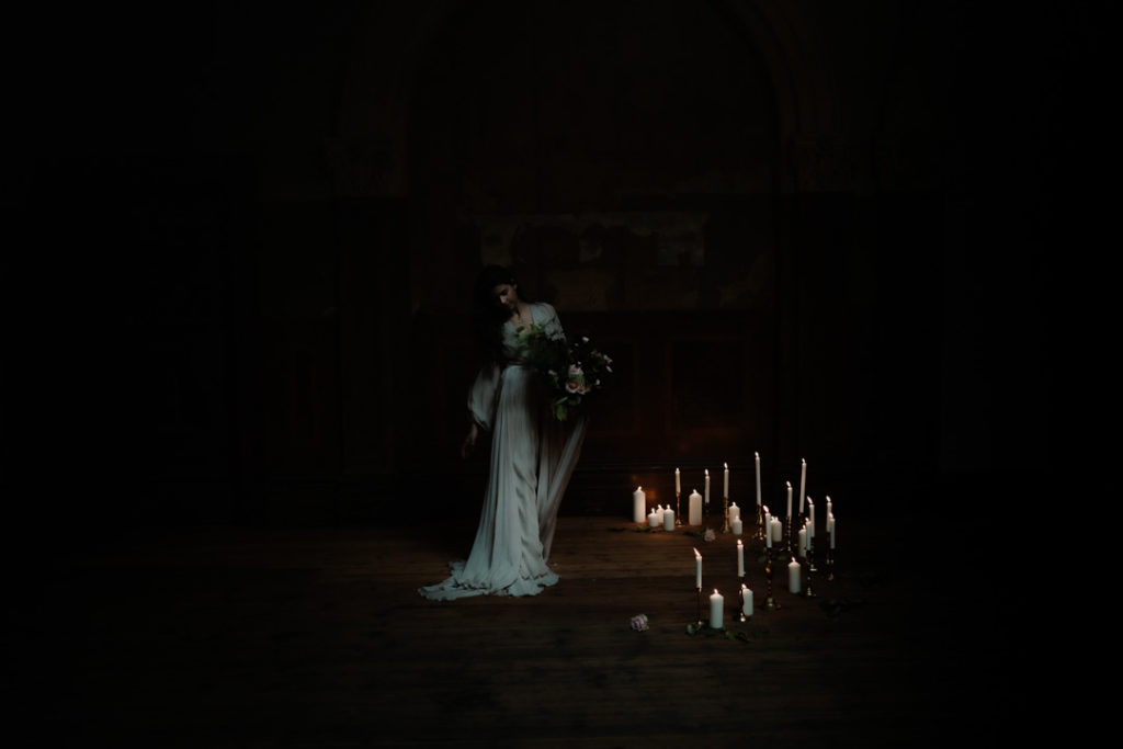 Bride dressed in Belinda Pieris and Leanne Marshall holding a bouquet by Libertine Florist Bendigo with candles surrounding her at the altar.